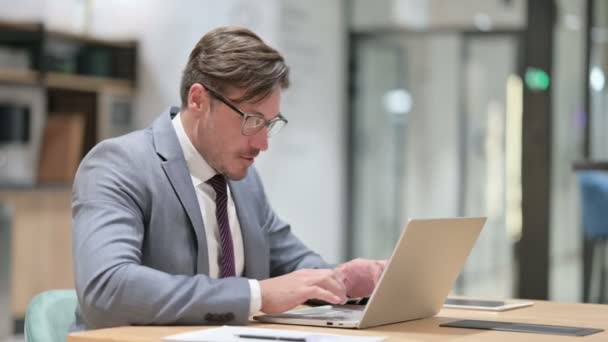 Возбужденный бизнесмен празднует успех на ноутбуке в офисе — стоковое видео
