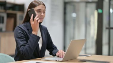 Dizüstü bilgisayarlı iş kadını Ofiste Smartphone 'da konuşuyor 