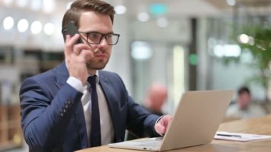 Dizüstü bilgisayarlı bir iş adamı iş yerinde Smartphone ile konuşuyor 
