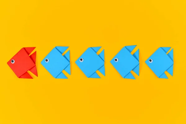 红色折纸鱼在一排排黄底蓝鱼面前游来游去 发现的概念和强有力的领导 — 图库照片#