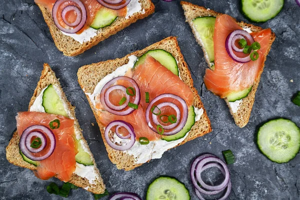 Somon ekmeği dilimleri sağlıklı kepekli tost üzerine füme somon balığı, kırmızı soğan ve taze soğan ve yaban turpu üzerine salatalık. 
