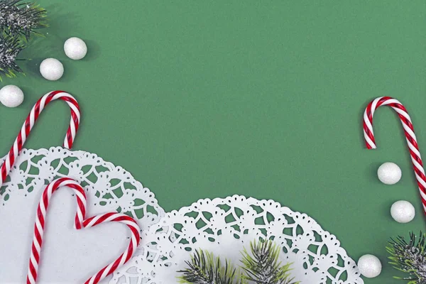 白いレースと季節のクリスマスフラットレイ毎日 緑のコピースペースの背景に雪の玉と伝統的なキャンディーの杖とモミの枝 — ストック写真