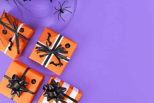 Gift boxes with traditional Halloween event colors orange, black and white and small bats and pumpkins and spider on purple background with empty copy space