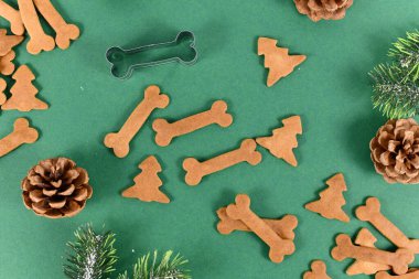 Ev yapımı fırınlanmış köpek manzarası, çam kozalaklı şenlikli yeşil arka planda, kemik şeklinde kurabiyeler ve Noel ağacı ikram ediyor.