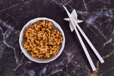 'natto' nun en üst görüntüsü, geleneksel Japon yemekleri mayalanmış soya fasulyesi kasesinde, yemek çubuklarıyla koyu arka planda yapılır.