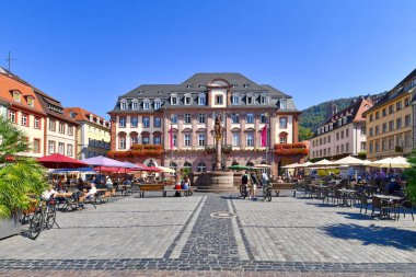Heidelberg, Almanya - Eylül 2020: Pazar yerindeki tarihi belediye binası önünde çeşme ve heykel ve güneşli bir günde açık hava kafelerinde oturan insanlar