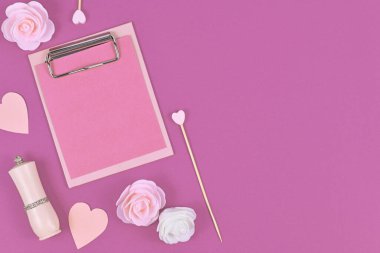 Boş pano ve gül çiçekleri, ruj ve boş fotokopi alanı olan pembe arka planda kağıt kalplerle yatıyordu.