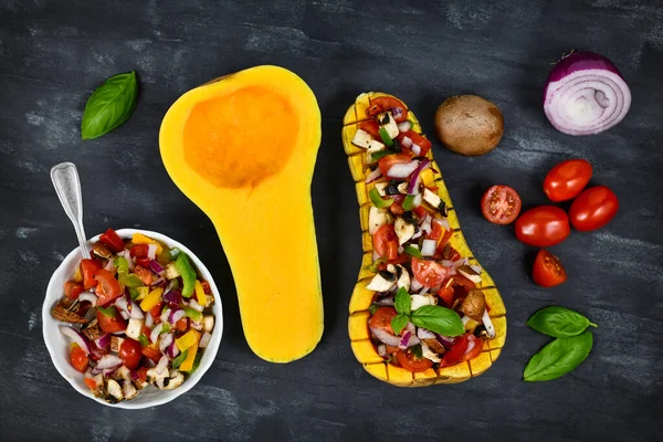 Vegan baked Butternut squash filled bell pepper, cherry tomatoes, red onion and mushrooms surrounded by ingredients on dark background
