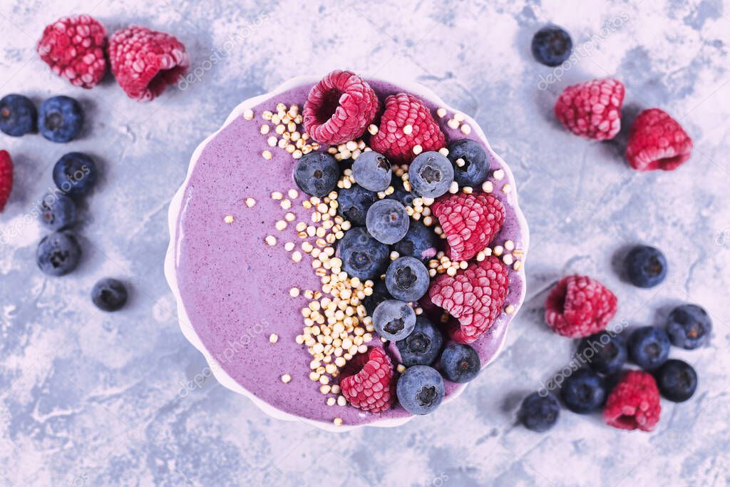 Healthy fruit smoothie bowl with yogurt decorated with raspberry, blueberry and puffed quinoa grain on gray background, top view