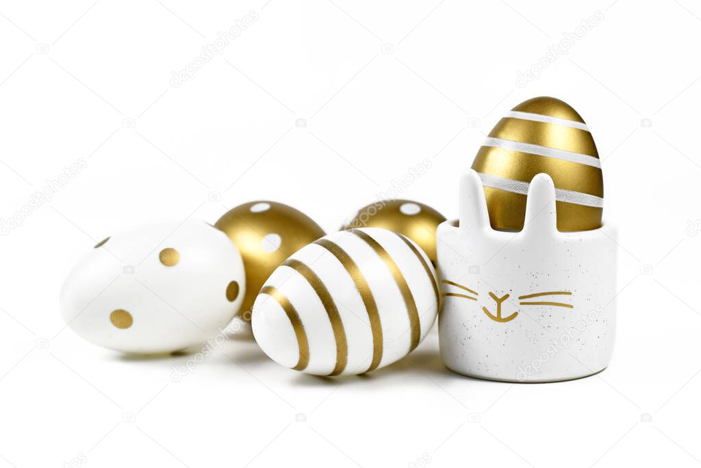 Painted easter eggs with metallic golden and white stripes and dots and cute easter egg cup in shape of bunny on white background
