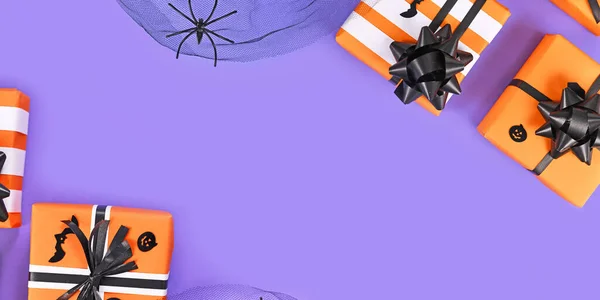 Banner with gift boxes with traditional Halloween event colors orange, black and white and spider on purple background with empty copy space in middle