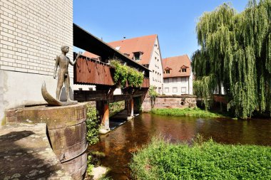 Ettlingen, Almanya - 13 Ağustos 2025: Alb Nehri üzerinde ahşap köprüsü ve balık tutan insan heykeli bulunan tarihi Ettlingen kasabası