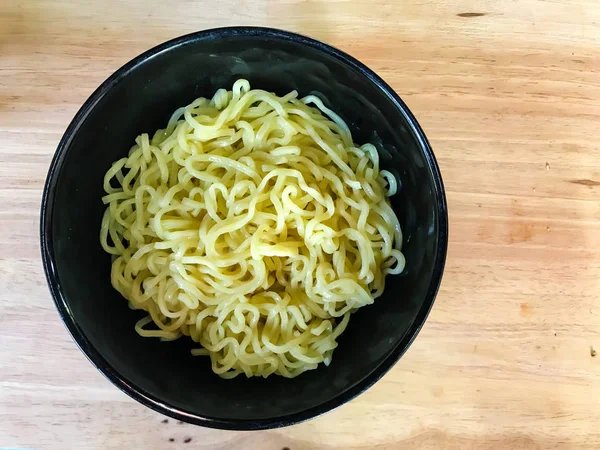 Noodles in a black bowl on wooden background — Stock Photo, Image