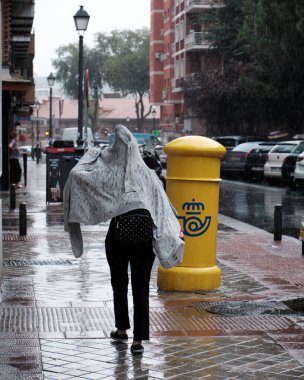 Madrid, İspanya: 17 Eylül 2020. Yağmurda yürüyen ve başını ceketiyle örten bir kadın.