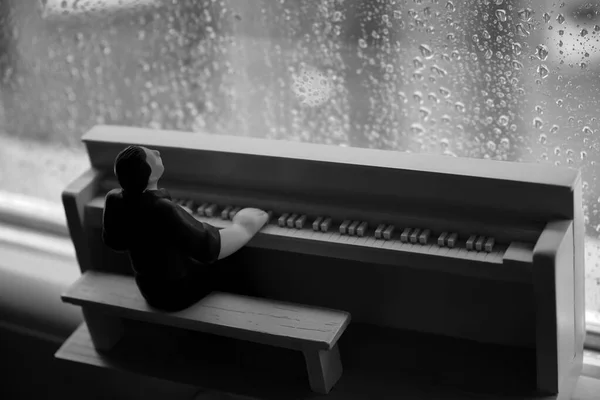 Drewniana postać mężczyzny grającego na pianinie za szybą w deszczu — Zdjęcie stockowe