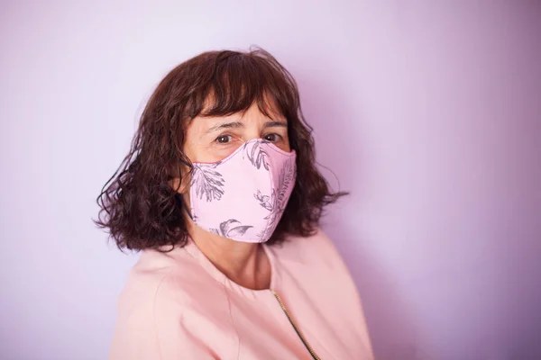 Middle age curly hair woman wearing pink medical mask on a pink background