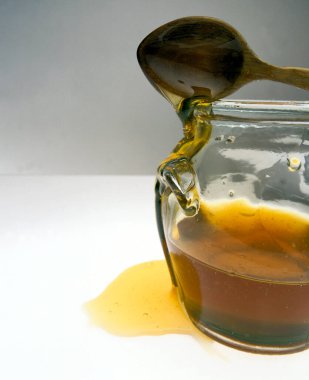 Beyaz arka planda cam kavanoz bal ve tahta kaşık.