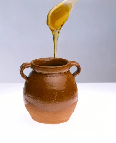 honey in a clay jug and wooden spoon on white background