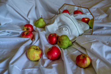 Antik Yunan heykeli beyaz alçı David 'in kırmızı sarı elmalar ve yeşil armutlar arasındaki göz kaplaması bir çerçevede bir aynaya yansıyor beyaz örtülü ve kıvrımlı arka plan 