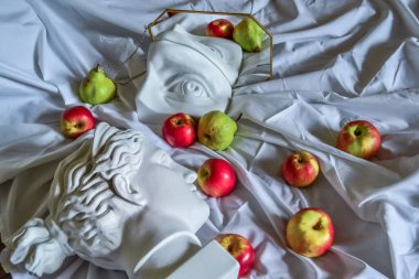 Antik Yunan beyaz heykeli, Diana 'nın alçı heykeli, David' in gözü, altın çerçeveli bir aynaya yansıyan, kırmızı elmalı ve yeşil armutlu beyaz kumaşın arka planına karşı.