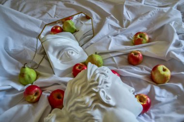 Antik Yunan beyaz heykeli, Diana 'nın alçı heykeli, David' in gözü, altın çerçeveli bir aynaya, yeşil armut ve sarı elmalı katlanmış beyaz kumaştan oluşan bir arka plana yansıyor.