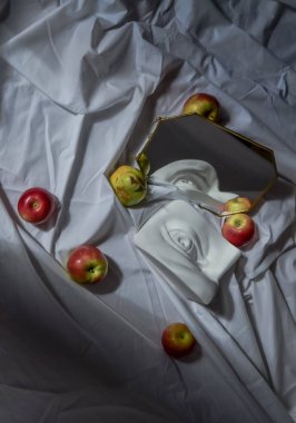 Antik Yunan beyaz heykel alçı mermer mermer David 'in altın çerçeveli aynaya yansıyan gözü kırmızı elmalar ve yeşil armutlarla kaplı beyaz kumaş kumaşın arka planına karşı