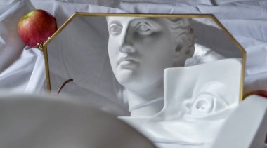 Antik Yunan heykeli Diana 'nın beyaz mermer kafası ve David' in gözü bir çerçevedeki aynaya yansıyan beyaz kumaş örtüsü ile elmalı katlar.