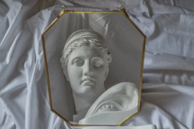 Antik Yunan heykeli, Diana 'nın beyaz alçı mermer kafası ve David' in gözü, bir çerçevedeki aynaya yansıyan beyaz kumaş örtüsünün arka planına karşı kıvrımlı.