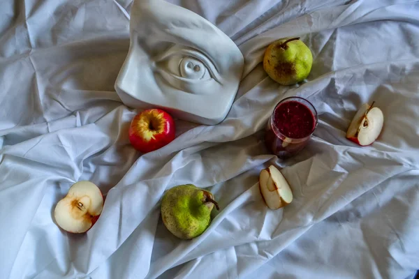 Antik Yunan heykeli beyaz alçı David 'in arka plandaki kırmızı elmalar ve yeşil armutlarla beyaz kumaş örtüsüne karşı.