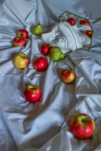 Antik Yunan heykeli, Diana 'nın beyaz alçı mermer kafası ve David' in gözü, çerçevedeki aynaya yansıyan kırmızı elmalı ve yeşil armutlu beyaz kumaşın arka planına karşı.