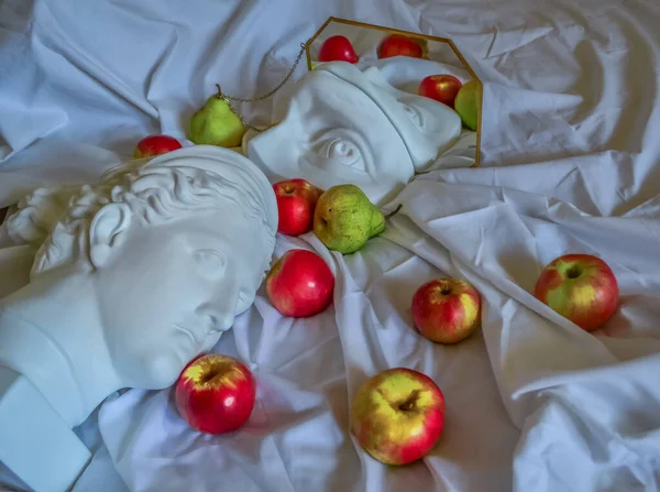 Antik Yunan beyaz heykeli, Diana 'nın alçı heykeli, David' in gözü, altın çerçeveli bir aynaya, yeşil armut ve kırmızı elmalı katlanmış beyaz kumaştan oluşan bir arka plana yansıyor.