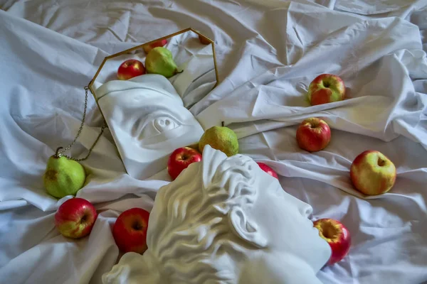 Antik Yunan beyaz heykeli, Diana 'nın alçı heykeli, David' in gözü, altın çerçeveli bir aynaya, yeşil armut ve sarı elmalı katlanmış beyaz kumaştan oluşan bir arka plana yansıyor.