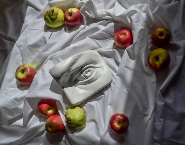 Ancient greek sculpture white plaster marble eye of david against a background of white drapery fabric with folds with green pears and red apples