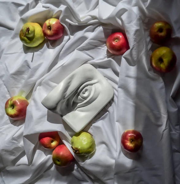 Antik Yunan heykeli beyaz alçı mermer mermer David 'in arka plandaki yeşil armut ve kırmızı elmalarla beyaz kumaş örtüsüne karşı 