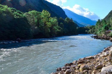 Dağlık mavi bir nehir tepeler ve dağlar arasında akar yeşil ağaçlar ve çalılarla kaplıdır.