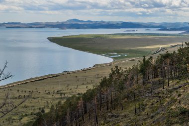 Baykal Körfezi 'nin tepesinde adalar, yarımadalar, bulutlar, mavi dağlar ve güneş ışığında yeşil ağaçlarla çevrili tepeler.