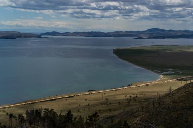 Baykal Körfezi 'nin en üst manzarasında adalar, yarımadalar, dağlar ve tepeler güneş ışığında yeşil ağaçlar, aşağıdaki yol.