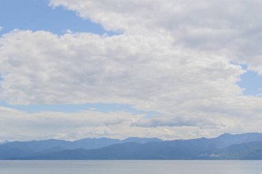 Baykal Gölü 'nün dalgalı sularının berrak, ufukta mavi dağlar, arka planda beyaz, yumuşak bulutlar.