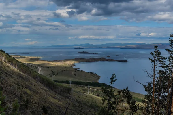 Baykal Körfezi 'nin tepesinde adalar, yarımadalar, yağmur bulutları, dağlar ve güneş ışığında yeşil ağaçlarla çevrili tepeler.