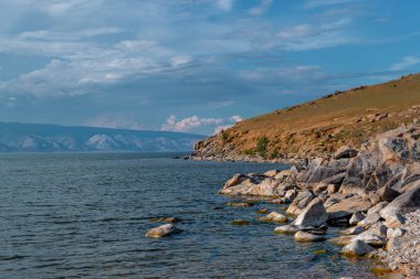 Batan güneşin ışığında turuncu büyük taşlar, kıyıda körfez, Baykal Gölü kıyısında kıyı, dağlarda arka plan