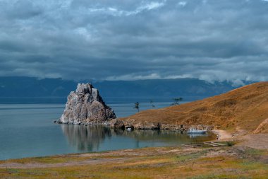 Mavi Baykal Gölü 'ndeki Cape Shamanka kayası otlak bozkırların arasında, büyük dağların ve yağmur bulutlarının arka planında, sahil şeridinde