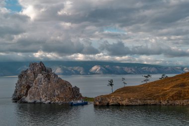 Cape Shamanka kayası berrak mavi Baykal Gölü 'nde dağların arasında güneş ışığı ve bulutların arasında.