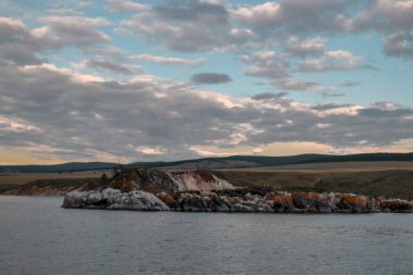 Baykal Gölü 'nde büyük bulutlarla sıcak bir akşam, yamaçlı Rocky kayalık kıyısı.