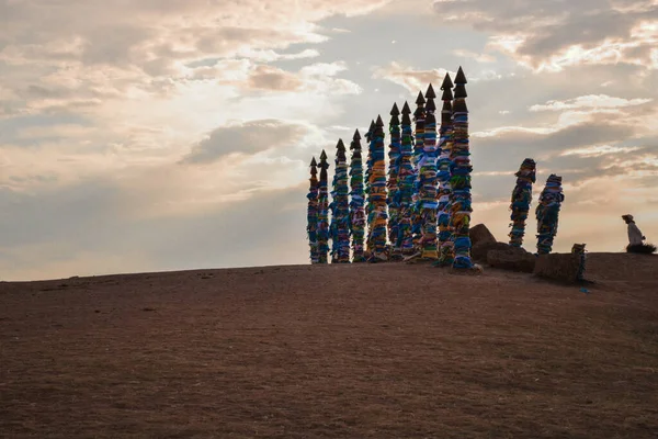 Olkhon Adası 'ndaki Baykal bozkırında, arka planda, renkli kurdelelerle bağlanmış yüksek ayin sütunları ve sıcak bir günbatımı gökyüzü.