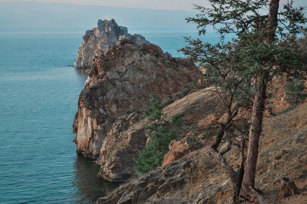 Mavi Baykal Gölü 'ndeki Şamanka Burnu çimenli taşların arasında kozalaklı karaçam ağaçları olan turuncu kayalar, açık uzayın arka planı.
