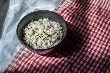 Beyaz kavrulmuş siyah pirinç, siyah bir bardakta, bir tabakta, kırmızı-beyaz bez havluların arka planında, güneşin altında, masanın üstünde bir gölgeyle.