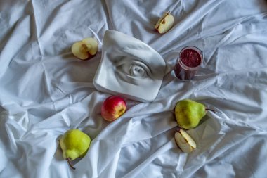 Olgun yeşil armut kırmızı elma püresi cam ve David 'in göz heykeli beyaz kumaş üzerinde güneş ışığı altında kıvrılmış.