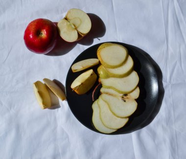 Armut ve elmanın parçalarını siyah bir tabakta kes. Güneşin ışığında beyaz kumaşın arka planına karşı.