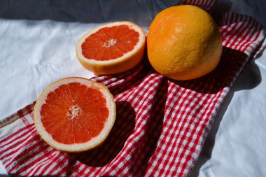 İki yarım kırmızı turuncu greyfurt ve beyaz kumaşla kaplanmış kırmızı kumaş. Güneş ışığı ve gölgeler.