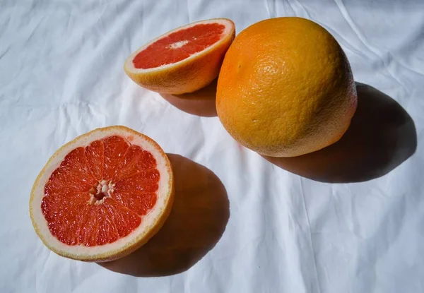 在白布上切下鲜亮的橙红色柚子 在阳光和阴影下折成褶皱 — 图库照片